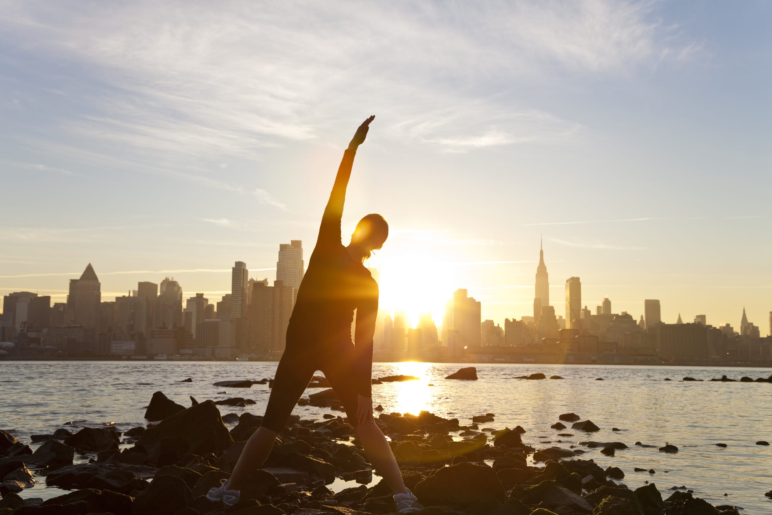 A woman runner stretching in a yoga position in front of the Manhattan skyline, New York City, United States of America, at early morning dawn sunrise